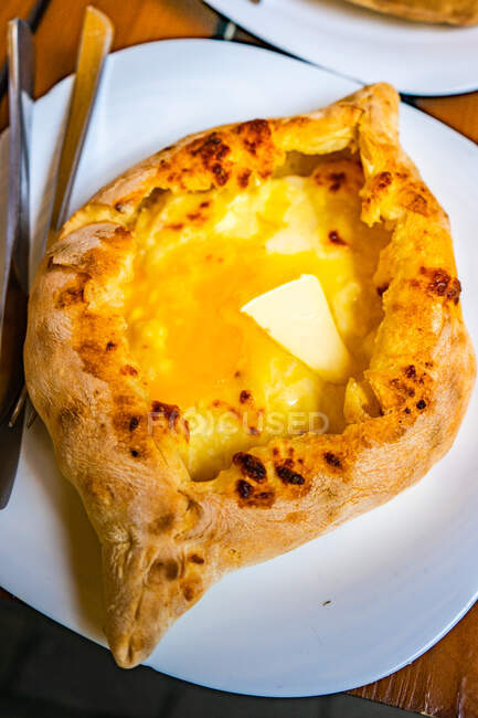 Khachapuri aiutante con formaggio, prosciutto, tuorlo d'uovo e burro sul piatto con posate — Foto stock