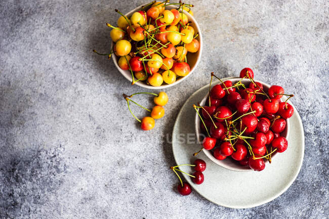 Schalen mit roten und gelben Kirschen auf Betonoberfläche, Draufsicht — Stockfoto