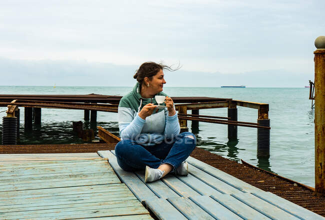 Smiling woman sitting on a pier drinking coffee, Batumi, Georgia — Stock Photo