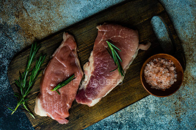 Vue de dessus des steaks de porc cru au romarin et au sel d'himalaya rose — Photo de stock
