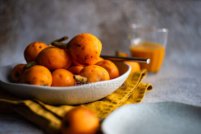 Bowl of loquats and fruit on cloth napkin and juice in glass — Stock Photo