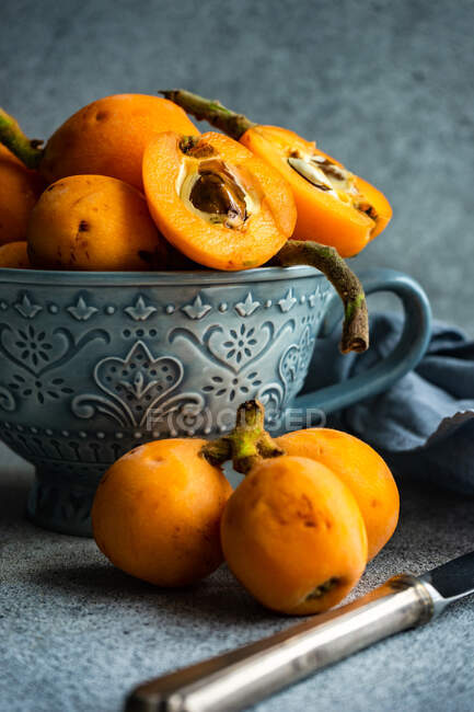 Fresh loquats in mug and on table with cloth napkin and knife — Stock Photo