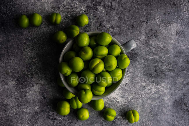 Mug of green plums on concrete surface, top view — Stock Photo