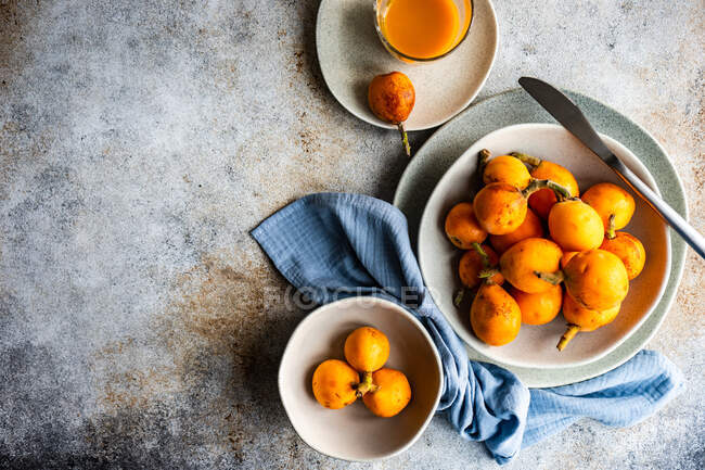 Top view of loquats and fresh juice on plates with cloth napkin and knife — Stock Photo