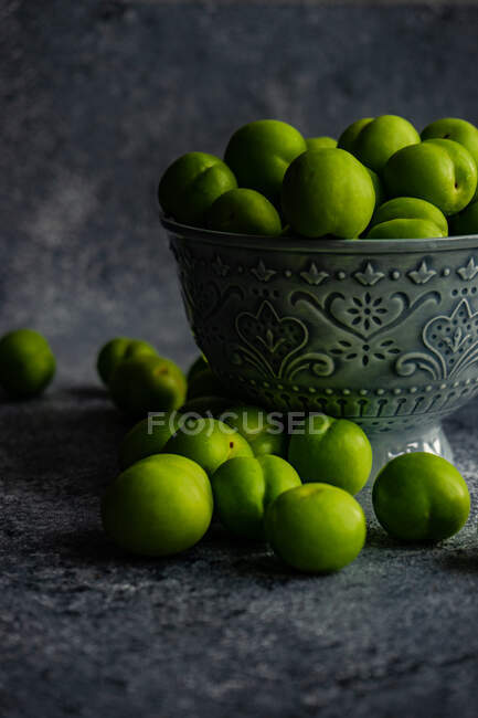 Bowl of green plums on concrete surface — Stock Photo