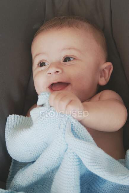 Close-up of a laughing baby boy holding a blanket — Stock Photo
