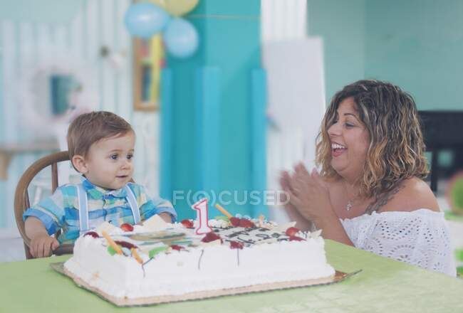 Mother and son sitting at a table with a first birthday cake — Stock Photo