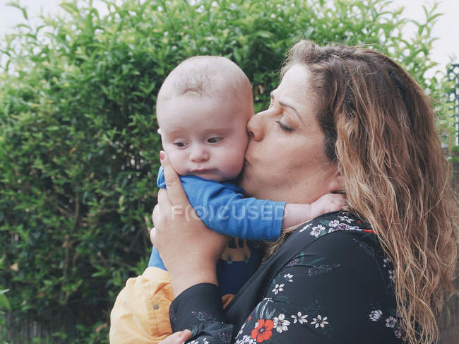 Madre in piedi in giardino baciare il suo bambino figlio — Foto stock