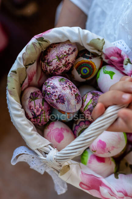 Primer plano de una persona que lleva una cesta con huevos de Pascua pintados - foto de stock