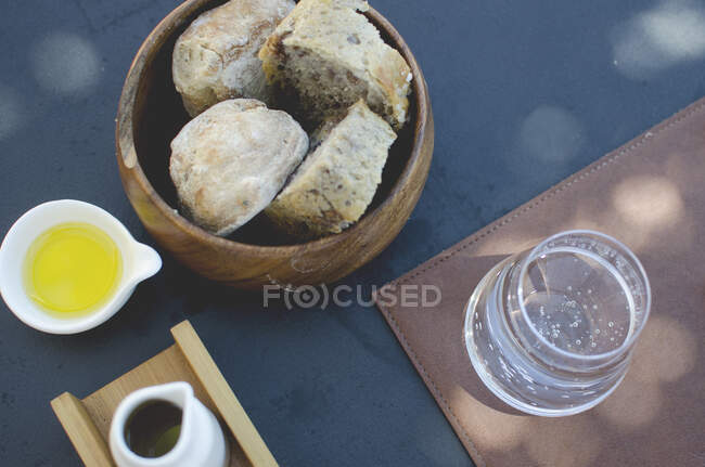 Vista aérea de una cesta de pan, aceite de oliva y un vaso de agua con gas - foto de stock
