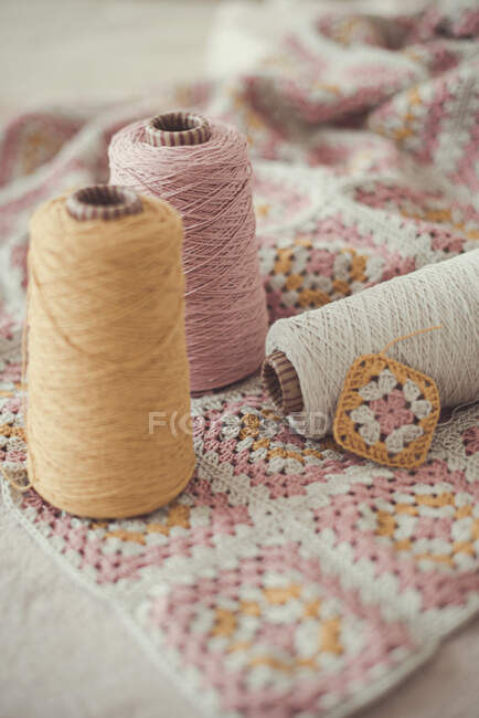 Close-up of three skeins of yarn and a crocheted patchwork blanket — Stock Photo