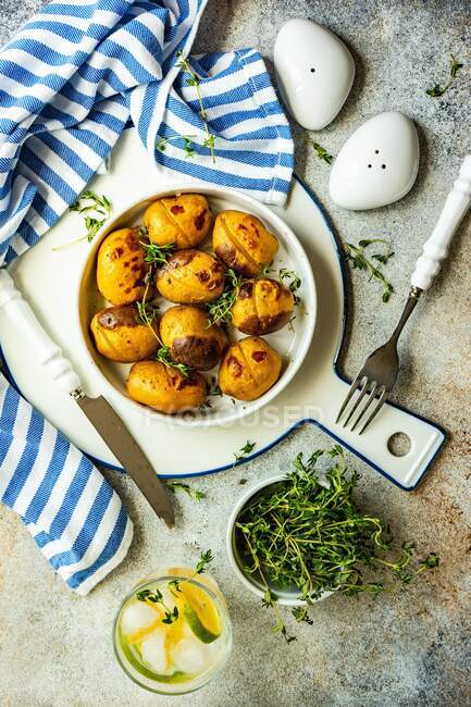 Overhead view of a bowl of roasted potatoes on a table with a glass of lemon ice water and thyme — Stock Photo