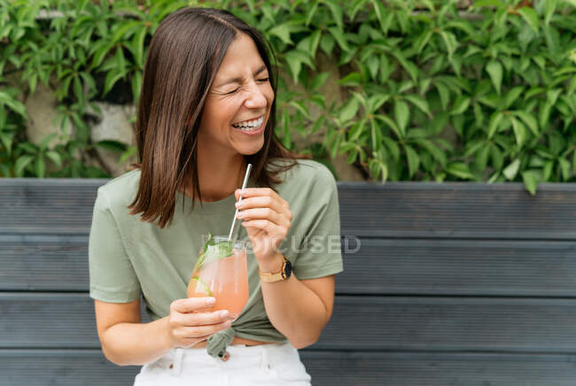 Портрет женщины с коктейлем из паломы, сидящей на скамейке и смеющейся — стоковое фото