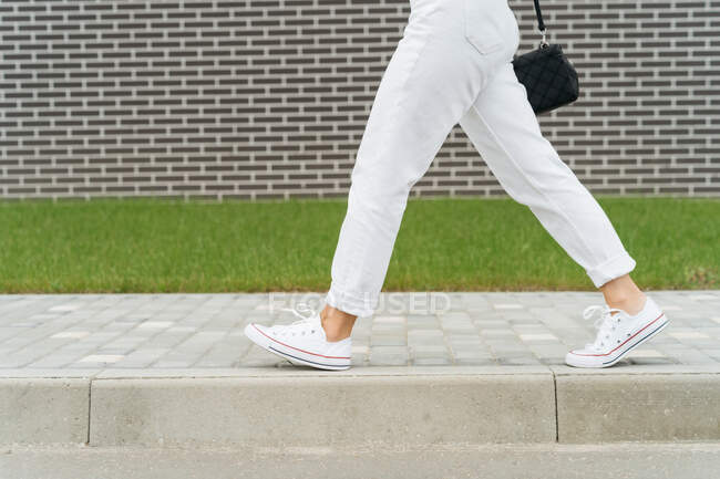Woman's legs in white trousers walking past a brick wall — Stock Photo