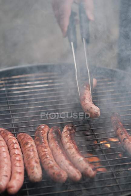 Homme retourner saucisses grillées sur un barbecue grill — Photo de stock