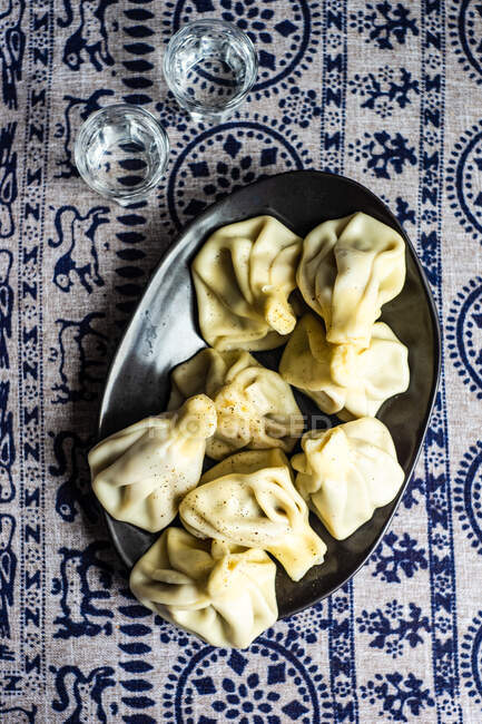 Khinkali dumplings served on plate with glasses of vodka on traditional covering Supra — Stock Photo
