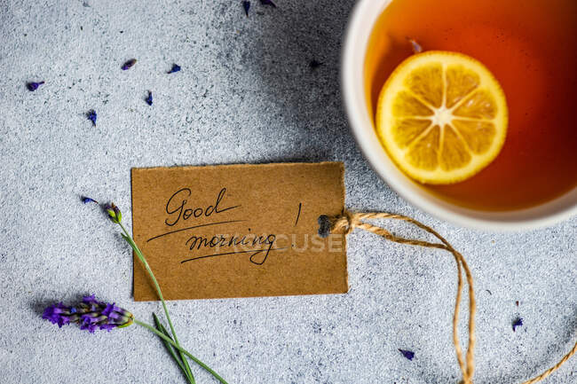 Xícara de chá de limão, flores de lavanda e bom dia tag no fundo de concreto — Fotografia de Stock