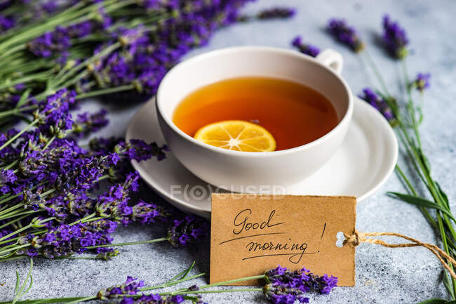 Tasse de thé au citron, fleurs de lavande et étiquette de bonjour sur fond de béton — Photo de stock