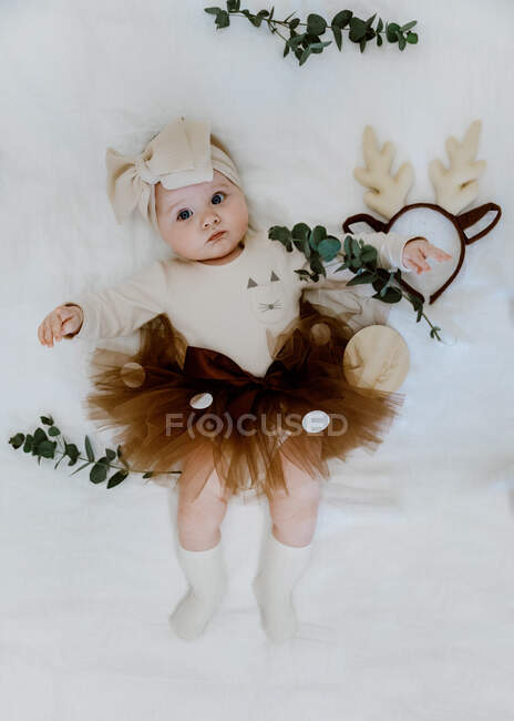 Overhead view of a baby girl dressed in a tutu lying on a bed surrounded by eucalyptus — Stock Photo