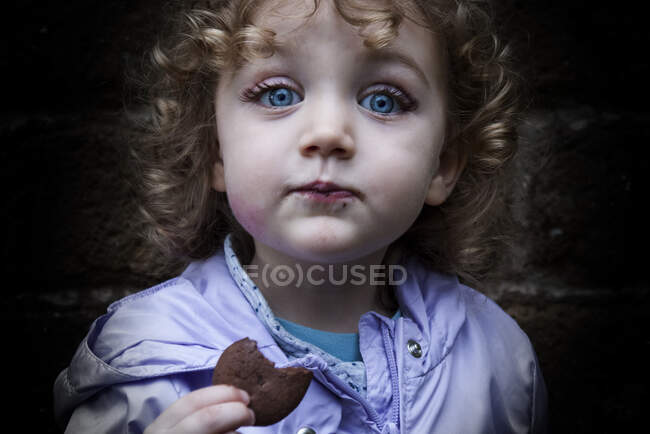Retrato de una chica sonriente comiendo una galleta - foto de stock