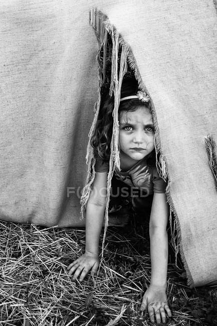 Menina séria olhando para fora de um interior de uma tenda rasgada — Fotografia de Stock