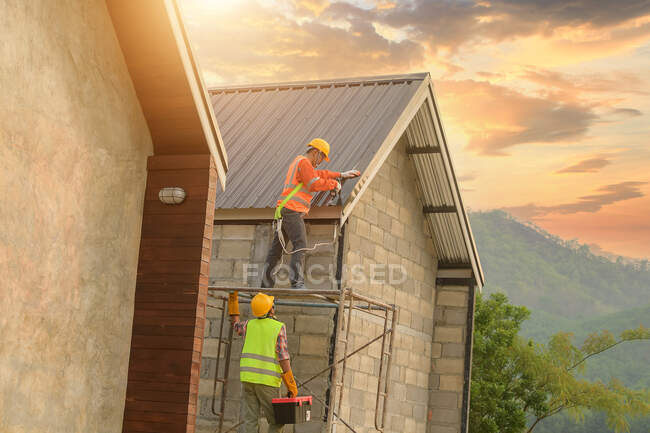 Два строителя устанавливают металлические листы на крыше, Таиланд — стоковое фото
