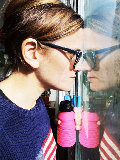 Nahaufnahme einer Frau, die durch ein Fenster blickt und ihr Spiegelbild — Stockfoto