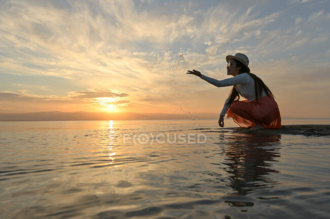 Щаслива безтурботна жінка, яка насолоджується чудовим заходом сонця на березі моря — стокове фото