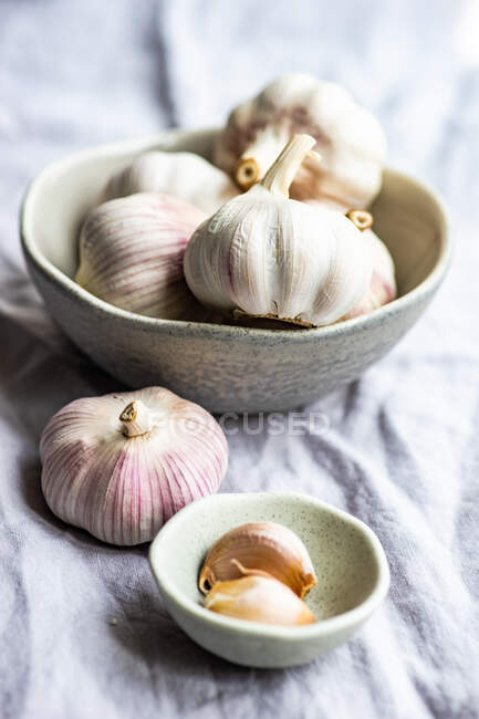 Raw garlic gloves in bowl on grey cloth background — Stock Photo