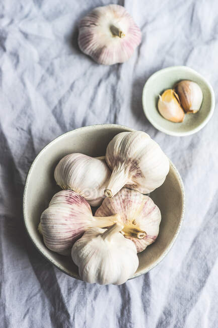 Raw garlic gloves in bowl on grey cloth background — Stock Photo