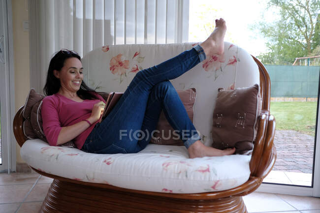 Mujer sonriente sentada en un sofá usando una tableta digital - foto de stock