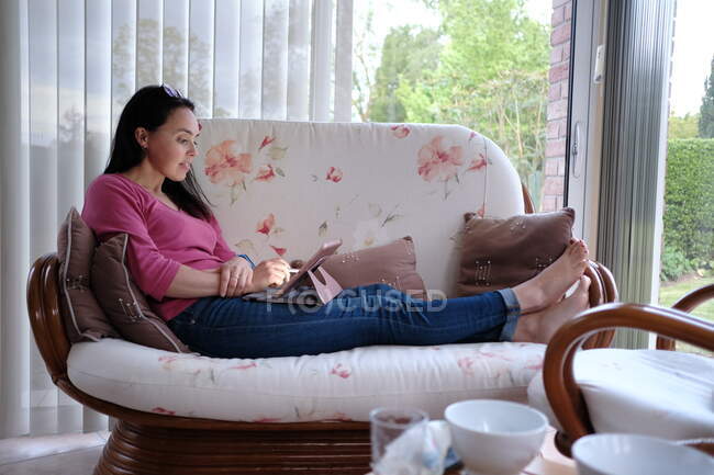 Жінка сидить на дивані за допомогою цифрового планшета — стокове фото