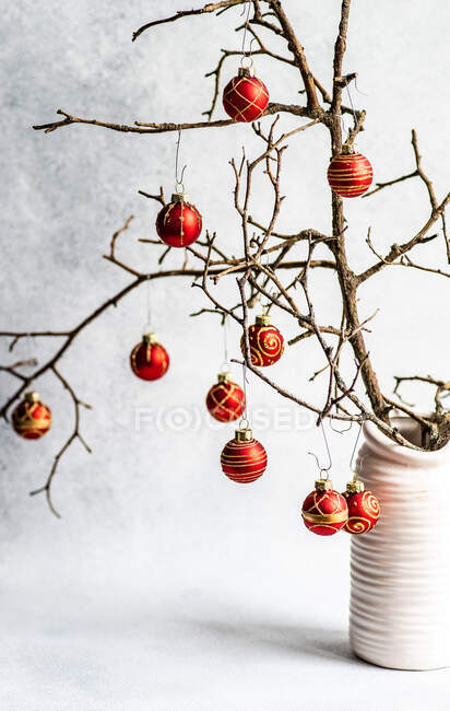 Concepto de tarjeta navideña con ramas secas decoradas con bolas rojas en interior de hormigón gris - foto de stock