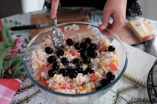 Крупним планом жінка готує рисовий салат з помідорами, солодким кукурудзою та оливками — стокове фото
