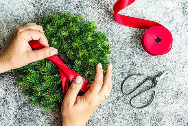 Overhead view of a woman tying a ribbon on a fir wreath — Stock Photo