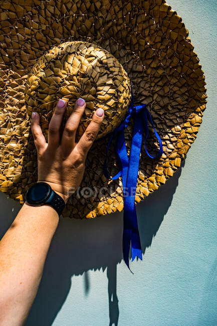 Woman's hand holding a straw hat against the wall — Stock Photo