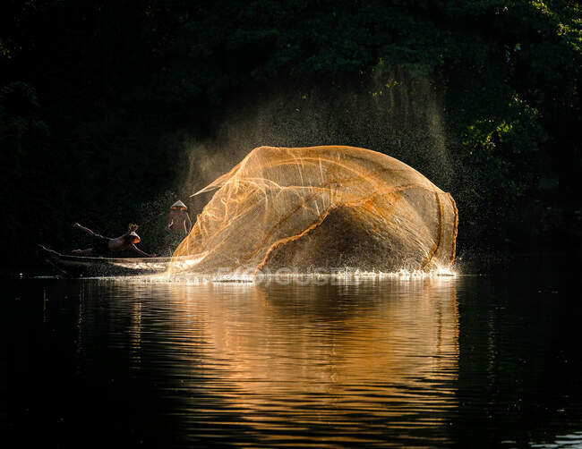 Zwei Fischer werfen in einem Boot ein Fischernetz in den Fluss, Vietnam — Stockfoto