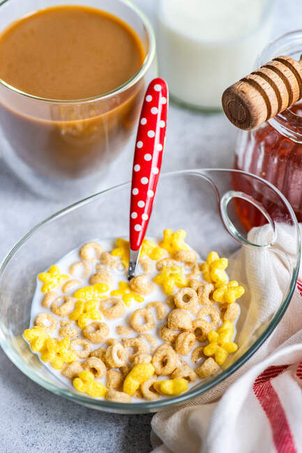 Cuenco de cereales, leche, miel y una taza de café en una mesa al lado de una toalla de té - foto de stock