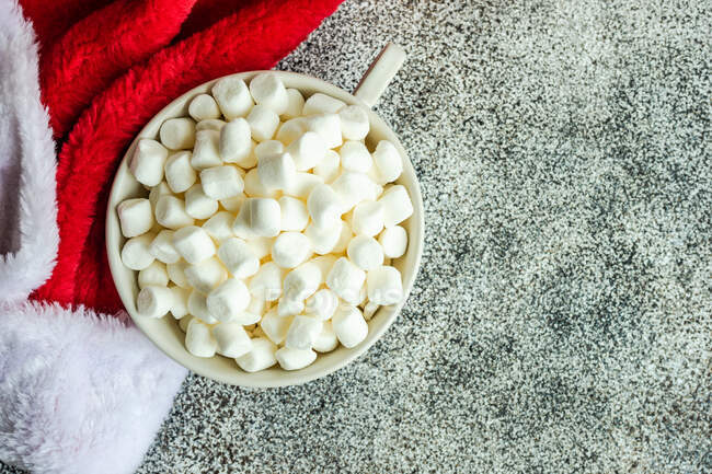 Overhead view of a mug filled with mini marshmallows next to a santa hat — Stock Photo