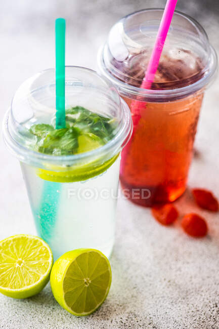 Клубничный лимонад и лайм с мятным лимонадом на столе со льдом, свежей лаймом и клубникой — стоковое фото