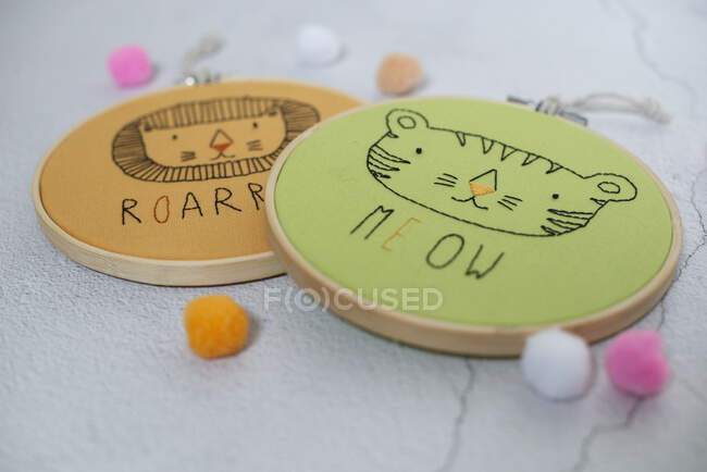Two embroidery hoops with lion and cat faces on a table — Stock Photo