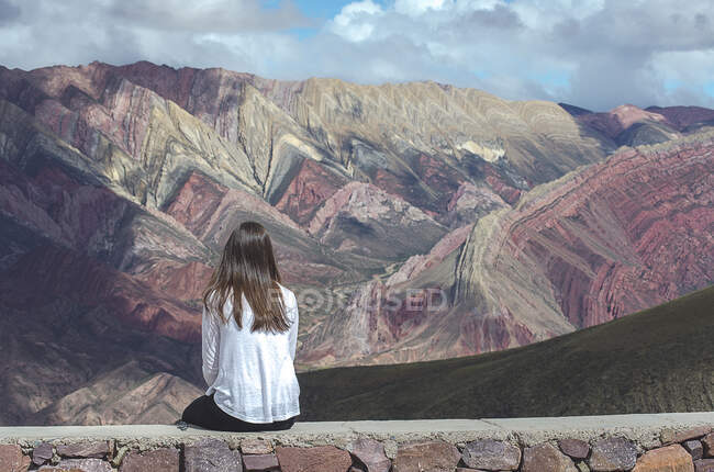 Visão traseira de uma mulher sentada em uma parede olhando para a paisagem da montanha, El Hornacal, Jujuy, Argentina — Fotografia de Stock