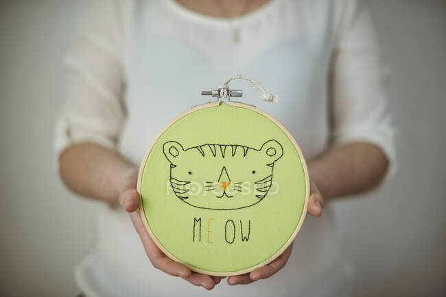 Woman holding an embroidery hoop with a cat's face and the word meow — Stock Photo