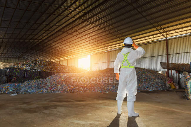 Visão traseira de um trabalhador manual em uma usina de reciclagem vestindo terno de risco biológico, Tailândia — Fotografia de Stock