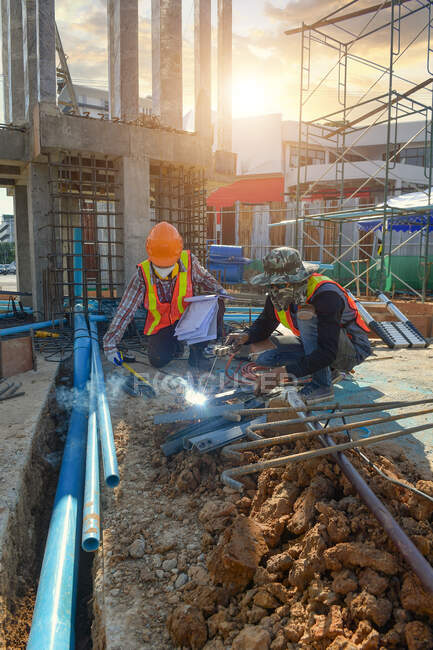Contremaître sur un chantier mesurant un morceau de métal et un ouvrier soudant un morceau de métal, Thaïlande — Photo de stock