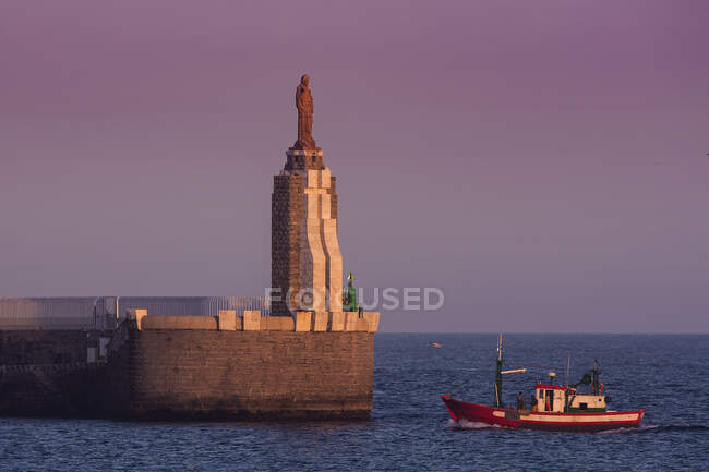 Bateau de pêche naviguant dans le port après la statue du Sacré-Cœur de Jésus et Punta del Santo au loin, Tarifa, Cadix, Andalousie, Espagne — Photo de stock