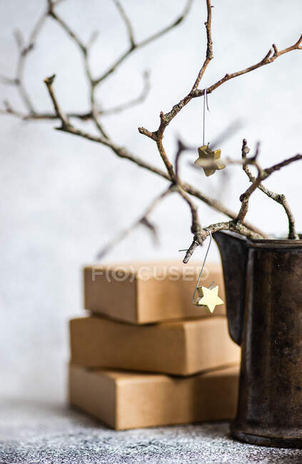 Stack of gifts next to Christmas branches with stars in a jug — Stock Photo