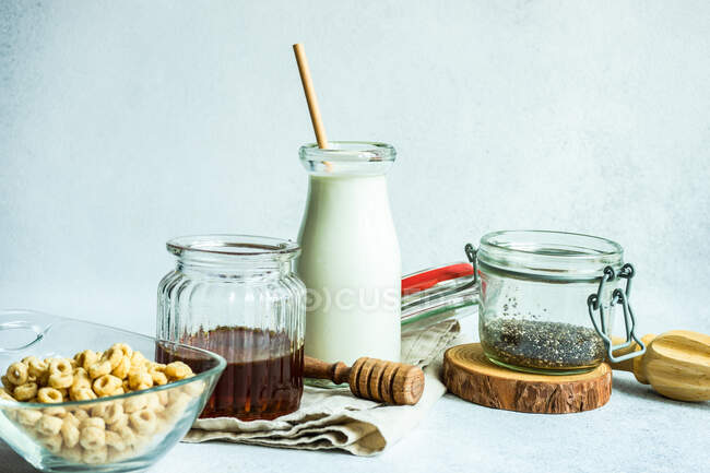 Cuenco de cereal junto a una botella de leche, semillas de chía y miel - foto de stock