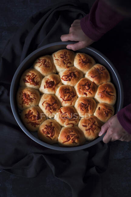 Вид зверху на людину, що тримає піднос для випічки, наповнений свіжоспеченими рулетами хліба — стокове фото