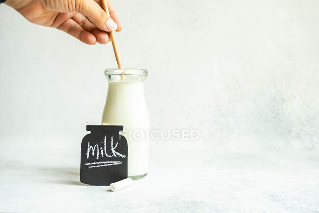 Mujer revolviendo una botella de leche de época junto a una pizarra con la palabra leche - foto de stock